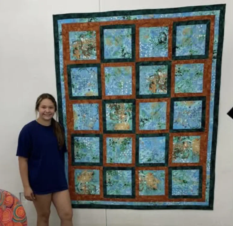 Young quilter beside a finished quilt on the design wall
