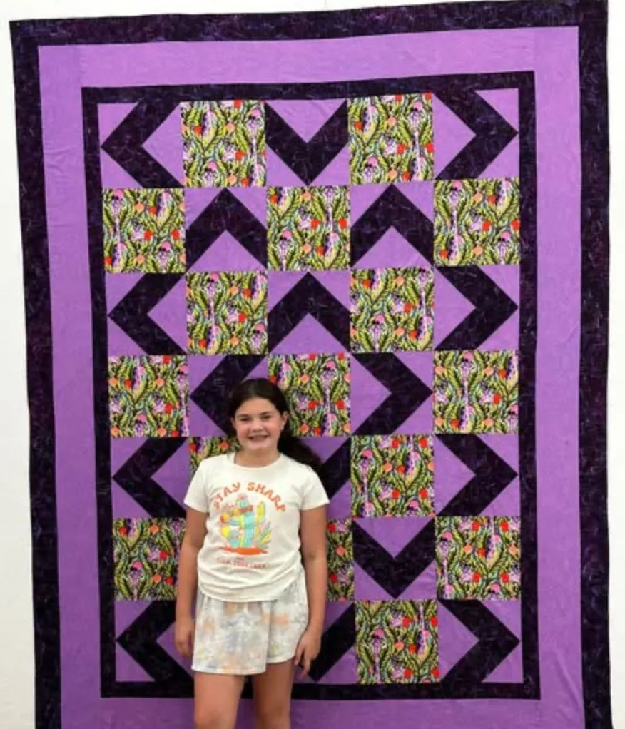 Young quilter in front of a finished quilt