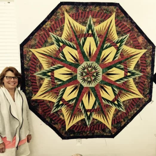 Guest with a large finished quilt on the design wall