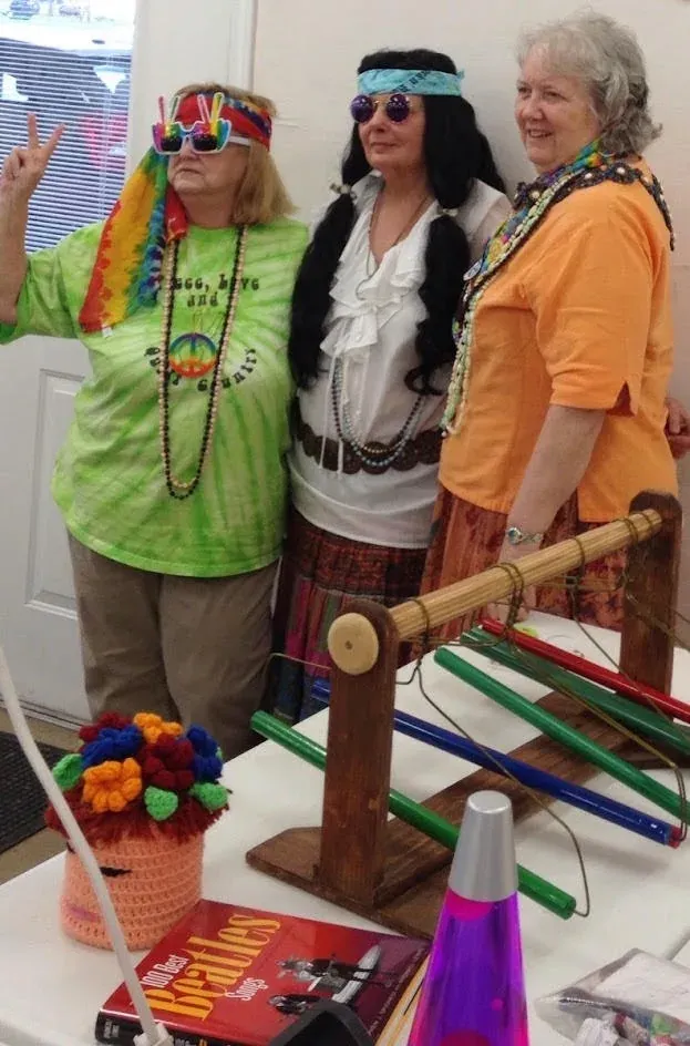Three guests in hippie costumes posing with peace-sign props