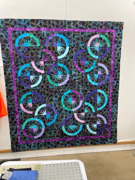 Teal and purple circular Mariner's Compass quilt pinned on the design wall