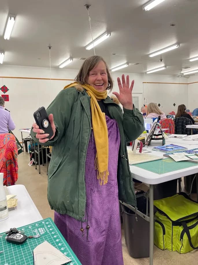 Guest bundled in a coat and scarf, holding purple fabric in the workroom